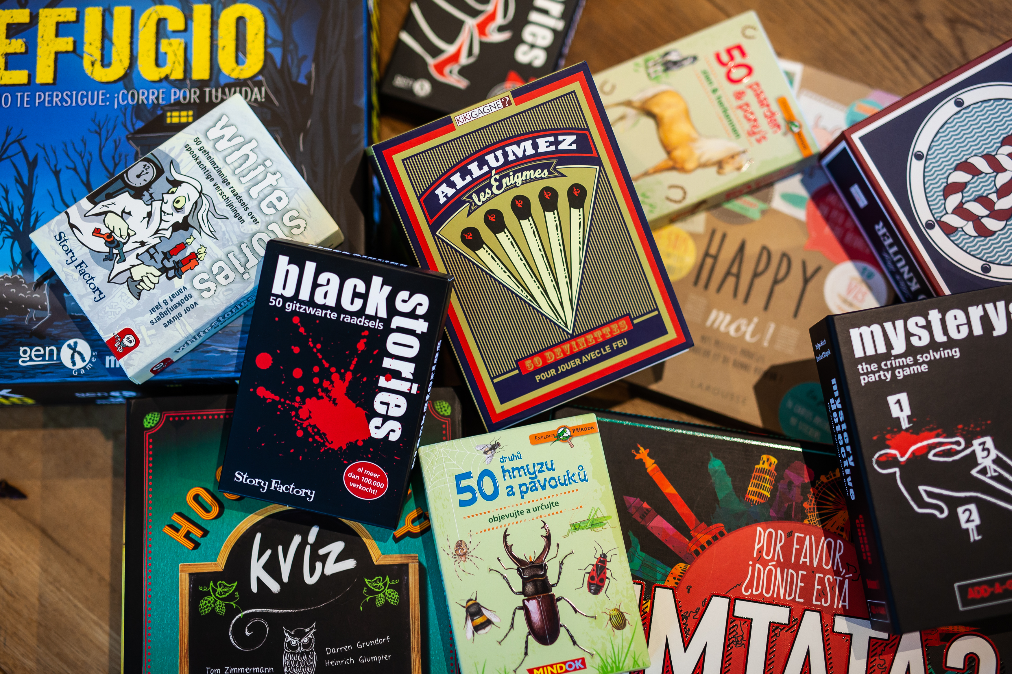 Mehrsprachige Rätsel- und Partyspiele auf Holztisch, darunter Black Stories und Allumez, Marke: moses. Verlag