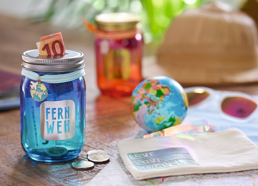 Sparglas mit 10-Euro-Schein und Aufschrift Fernweh, Globus, Sonnenbrille und Tuch mit Live Love Travel Marke: moses. Verlag